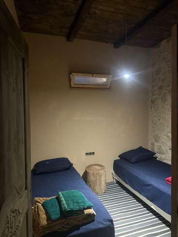 Esse quarto aconchegante tem duas camas de solteiro com roupa de cama azul-marinho, um tapete listrado, um banco de madeira, toalhas dobradas, pedras expostas e uma pequena janela no teto.