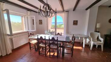 The image depicts a spacious room with a high ceiling, featuring a large window and a wooden floor, likely a living room or dining area, with a neutral color scheme and minimalist decor.