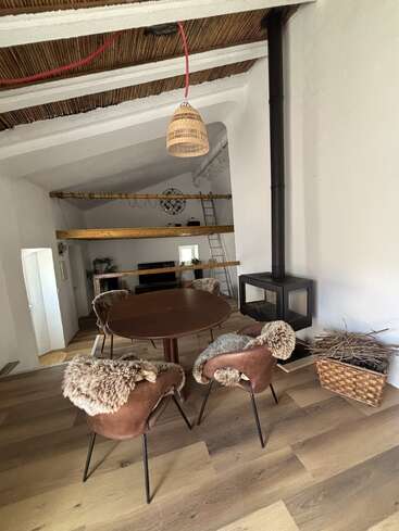 Esta acogedora habitación cuenta con una mesa redonda con cuatro sillas tapizadas de piel, una estufa de leña, una cesta de leña, un altillo y vigas de madera rústicas en el techo.