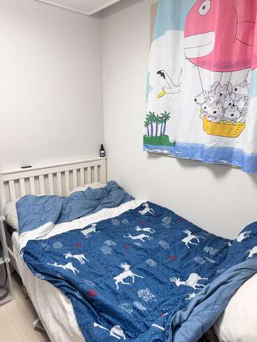 Um quarto pequeno e aconchegante com estrutura de cama branca, roupa de cama azul com veados brancos e um desenho colorido pendurado na parede com animais em um balão de ar quente.