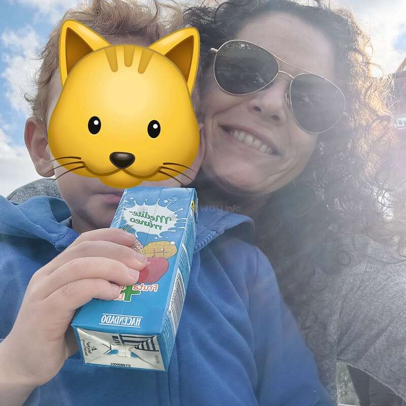 Das Bild zeigt eine Frau und ein Kind, die für ein Selfie posieren, wobei das Kind eine Saftbox hält und die Frau eine Sonnenbrille trägt.