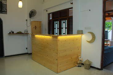 Cette image montre un espace d'accueil confortable avec un comptoir en bois, un éclairage chaleureux, des objets décoratifs, un ventilateur au mur et une étagère avec de petits objets.