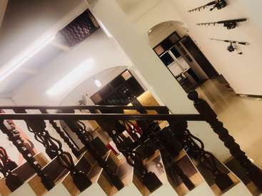 Cette image représente une scène d'intérieur avec un escalier en bois au premier plan, une lumière vive, des cannes à pêche accrochées au mur et un espace de vie confortable et spacieux.