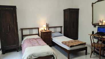 Cette chambre confortable dispose de deux lits simples, d'armoires en bois, d'une table de nuit commune avec une lampe, d'un bureau avec un ordinateur portable et d'un miroir mural décoratif.