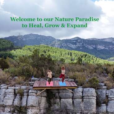 Deux personnes pratiquent le yoga sur une plate-forme en bois au-dessus de falaises rocheuses, entourées d'une forêt verdoyante et de montagnes. Au-dessus d'elles, le ciel affiche un message accueillant.
