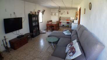The image depicts a living room with a couch, coffee table, and TV, featuring a large window and a fireplace, with a bookshelf and a dining table in the background.