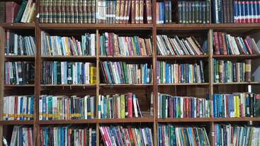 A large bookshelf filled with colorful books, neatly arranged in rows. The books vary in size and topics, creating a cozy, inviting library atmosphere.