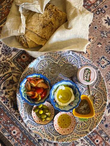 Un desayuno tradicional de Oriente Medio: pan plano, aceitunas, tomates, labneh rociado con aceite de oliva, especias za'atar, yogur, aceite de oliva, todo servido en una bandeja estampada.