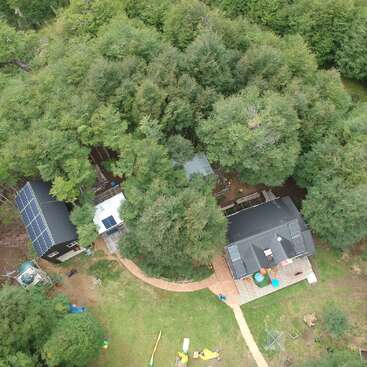 The image depicts an aerial view of a house and yard with a playground, surrounded by trees, featuring a deck, patio, and solar panels on the roof.