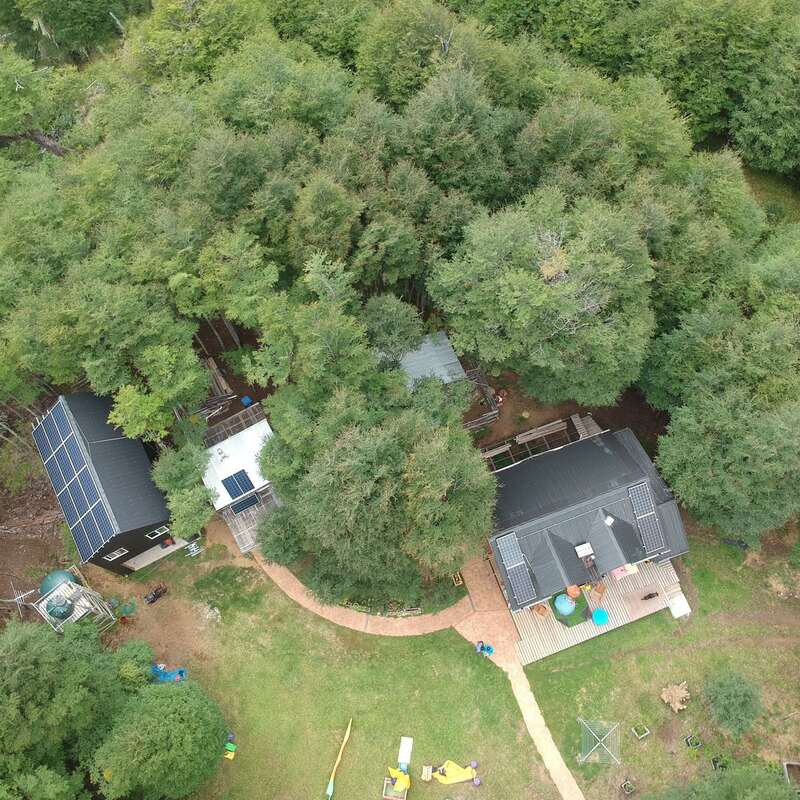 Das Bild zeigt eine Luftaufnahme eines Hauses und eines Hofes mit Spielplatz, umgeben von Bäumen, mit einer Terrasse und Sonnenkollektoren auf dem Dach.