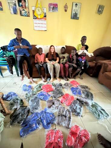 Un grupo de personas, entre las que hay niños y una mujer, están sentadas en un sofá, sonriendo. En el suelo hay numerosas zapatillas de colores.