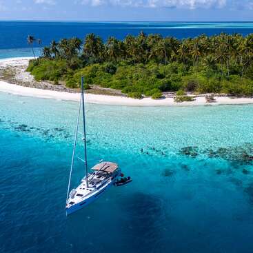 Eine kleine tropische Insel mit üppigen Palmen ist von klarem, türkisfarbenem Wasser umgeben. Ein weißes Segelboot liegt in der Nähe vor Anker und vervollständigt das Bild eines friedlichen Paradieses.