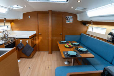 Cette photo montre l'intérieur chaleureux d'un bateau, avec une cuisine moderne, des murs en bois, des sièges rembourrés bleus, une table à manger dressée pour quatre personnes et un centre de table composé de fruits.