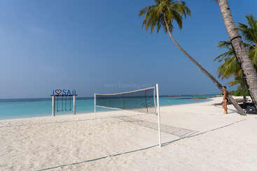 Une plage ensoleillée au sable blanc, un filet de volley-ball, des palmiers, une pancarte « I ♥ SAii » avec des balançoires, une mer d'un bleu limpide et une ambiance relaxante.