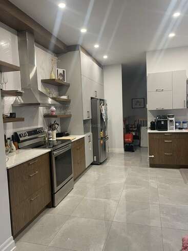 This modern kitchen features sleek cabinets, stainless steel appliances, and bright lighting. Open shelves display decor and glassware. A coffee station and fridge complete the organized space.