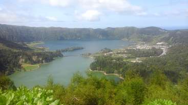 A imagem retrata uma paisagem serena com um lago, vegetação exuberante e um céu claro, evocando uma sensação de tranquilidade e beleza natural. A cena provavelmente se passa em uma área rural ou selvagem.