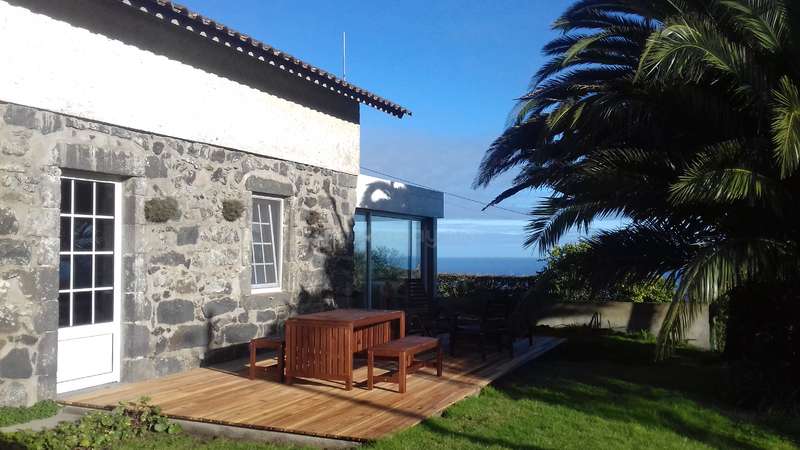 A imagem retrata uma cena serena ao ar livre, com uma casa com um grande quintal e uma piscina, cercada por árvores e arbustos, com um céu claro acima. A atmosfera é pacífica e idílica.