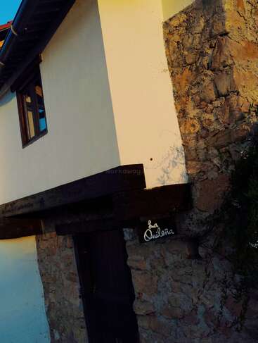 Un bâtiment rustique avec un mélange de plâtre blanc et de murs en pierre, des poutres en bois, une porte en bois sombre et un panneau indiquant "La Quileña" à l'entrée.