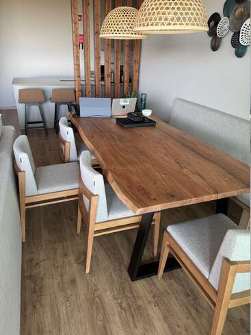 Ein gemütlicher, moderner Essbereich mit Holztisch, gepolsterten Stühlen, Laptops, Hängelampen, Wandkunst, Holzwand, Hockern und einer minimalistischen Einrichtung in Naturtönen.