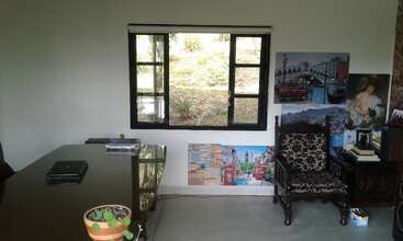 A tidy office with a large desk, black chair, potted plant, and window overlooking greenery. Wall art and a classic chair add a creative touch.