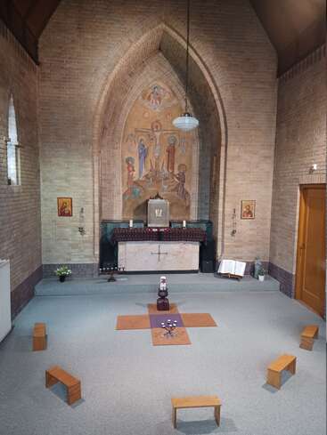 This image shows a small, peaceful chapel with a brick interior, altar, religious icons, benches arranged in a circle, and candles in the center.