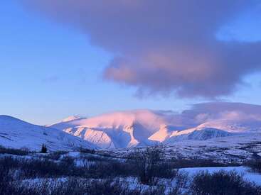 The image depicts a serene snowy mountain range with a few clouds in the sky, set against a backdrop of a clear blue sky.