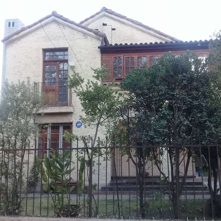The image depicts a two-story house with a beige exterior, brown trim, and a tiled roof, surrounded by trees and a black metal fence.