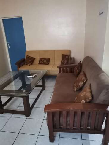 Cette image montre un salon simple avec deux canapés, une table basse en verre, des coussins à motifs, un sol carrelé, des murs unis et une porte bleue.