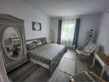 Cette chambre chaleureuse est équipée d'un grand lit avec une parure de lit à motifs, d'une élégante armoire avec miroir, d'un fauteuil confortable, d'un éclairage tamisé et d'une fenêtre ornée de rideaux.