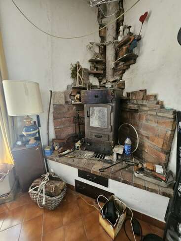 Ce coin confortable de la pièce est agrémenté d'un poêle à bois rustique encastré dans une alcôve en briques, entouré de bois de chauffage, d'outils, de décorations éclectiques, d'une lampe et d'étagères.
