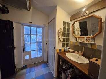 Cette image montre une salle de bain confortable avec un sol carrelé coloré, un lavabo en bois, un miroir octogonal, une décoration en briques de verre, une porte blanche et une vue extérieure à travers une porte vitrée.