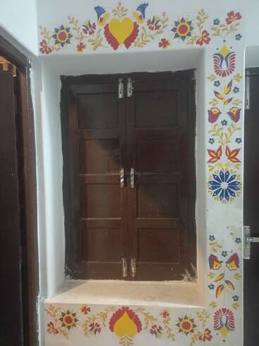 A dark wooden window is set in a white wall, beautifully bordered with colorful, traditional floral and heart-shaped folk art patterns, featuring red, yellow, and blue.