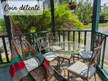 A cozy relaxation corner on a porch featuring a hammock chair, glass table with four chairs, greenery, sunlight, and a peaceful street view. "Coin détente" captioned.
