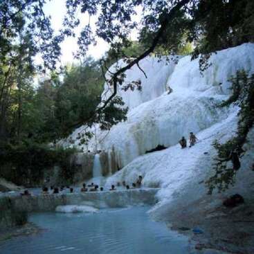 The image depicts a serene natural setting, featuring a large body of water, a waterfall, and a hillside covered in white rock, surrounded by lush greenery.
