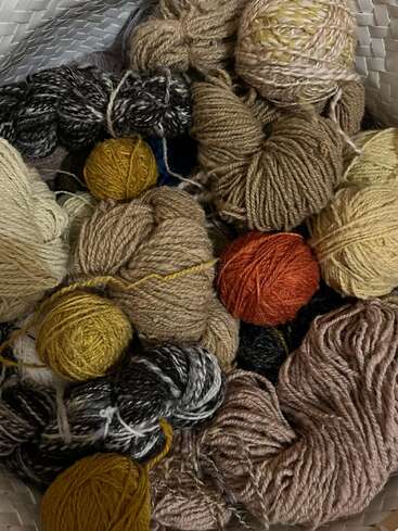 Un panier rempli de pelotes et d'écheveaux de fil dans des tons terreux, notamment beige, marron, jaune, noir et orange, démontrant les textures et la douceur.