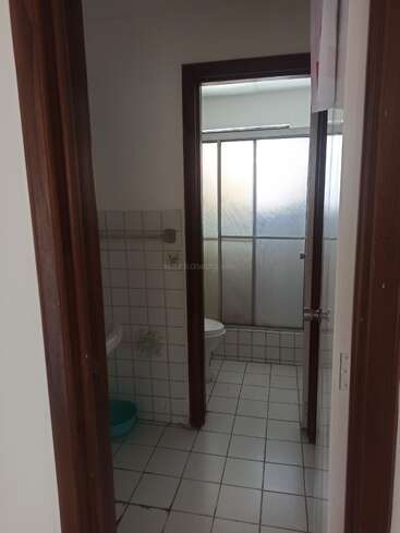 Das Bild zeigt ein schlichtes Badezimmer mit weiß gefliesten Böden und Wänden, einer Toilette, einem Waschbecken und einer Duschwand aus Milchglas im Hintergrund.