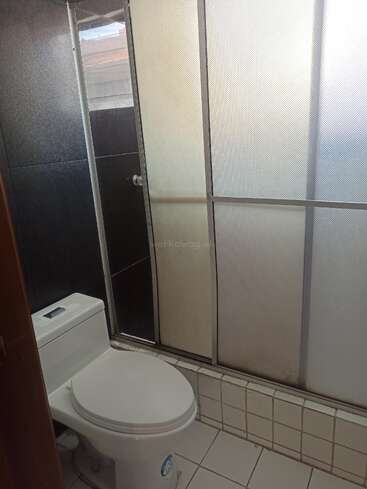 Das ist ein kleines Badezimmer mit einer weißen Toilette, Fliesenboden, schwarzen Wandfliesen und einer Duschkabine aus Milchglas mit Schiebetür. Schlichtes Design.