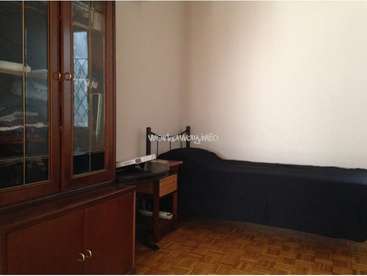 L'image représente une pièce avec une armoire en bois, un bureau et un canapé noir, avec un mur blanc et un sol en bois.