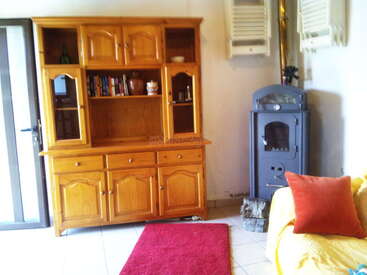 Un coin salon confortable avec une armoire en bois, des livres, un poêle à bois gris, un tapis rouge, un canapé jaune et un coussin rouge pour plus de confort.