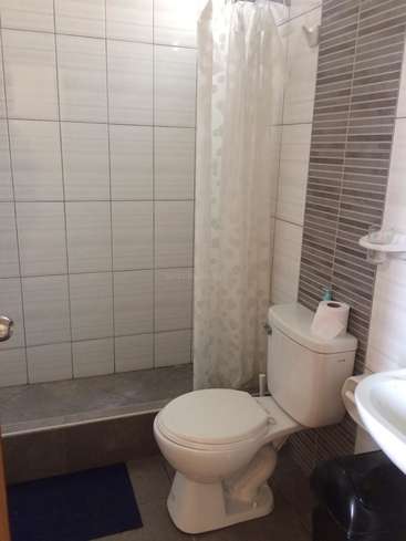 The image depicts a bathroom with a white toilet, shower, sink, and gray tiles on the floor and walls, featuring a white shower curtain and a blue mat.