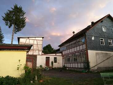 The image depicts a serene scene of two houses with a garden and trees, set against a cloudy sky, evoking a sense of tranquility and natural beauty.