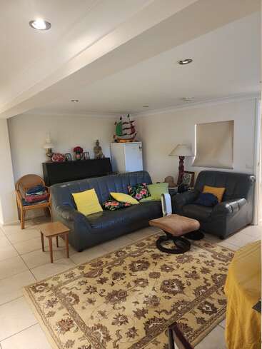 Dieses gemütliche Wohnzimmer hat zwei Ledersofas mit bunten Kissen, einen gemusterten Teppich, einen kleinen Kühlschrank, Lampen, Dekoartikel und eine warme, heimelige Atmosphäre.