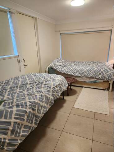 Dieses Bild zeigt ein kleines, aufgeräumtes Schlafzimmer mit zwei Einzelbetten, geometrisch blau gemusterter Bettwäsche, einem kleinen runden Tisch, gefliestem Boden und einem weißen Vorleger.