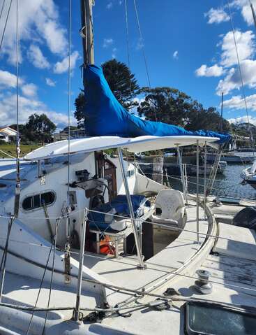 Ein weißes Segelboot, das unter einem strahlend blauen Himmel an einem Yachthafen angedockt ist, mit einer blauen Segelabdeckung, weißen Plastikstühlen und verschiedenen Bootsausrüstungen an Deck.