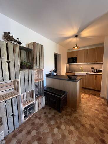 Esta acogedora cocina cuenta con armarios de madera, una moderna isla, suelo de baldosas hexagonales, estanterías de cajones con plantas, una lámpara colgante y un acento decorativo rústico en la pared.