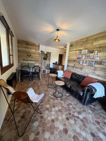 Este acogedor salón cuenta con paredes de madera rústica, un sofá de cuero con cojines, suelo de baldosas hexagonales, una silla mariposa, mesa de comedor, arte en la pared e iluminación colgante.