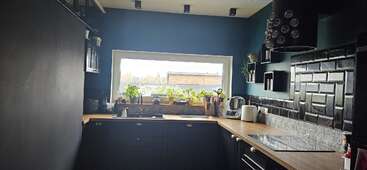 Esta moderna cocina cuenta con armarios oscuros, una encimera de madera y un salpicadero de azulejos negros. Una gran ventana deja entrar la luz natural, con macetas en el alféizar.