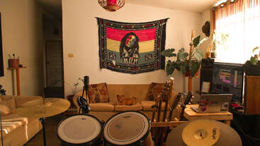 This cozy room features music equipment, guitars, and a drum set. A Bob Marley tapestry hangs above a sofa, with a small dog lounging comfortably.