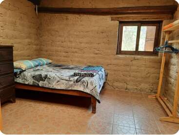 Dieses gemütliche, rustikale Zimmer verfügt über ein Einzelbett mit gemusterter Bettwäsche, eine Kommode aus Holz, einen schlichten Kleiderständer, einen Fliesenboden und ein kleines Fenster, durch das Tageslicht hereinfällt.