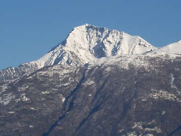 Un majestueux sommet montagneux se dresse, couvert de neige, dans un ciel bleu limpide. Les pentes inférieures sont plus sombres, partiellement recouvertes de neige, créant un contraste saisissant.